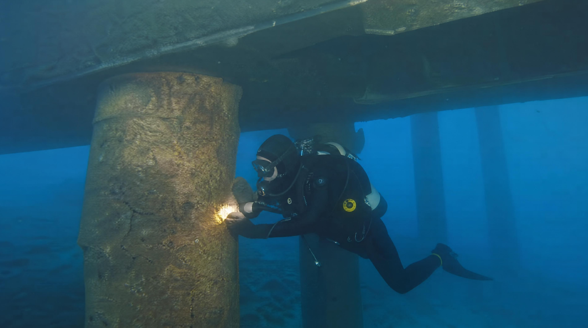 Plongeur professionnel en inspection sous-marine d'une pile de pont en béton, évaluant l'état structurel et les fissures pour un diagnostic technique.